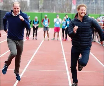 Two men smiling and racing on a running track, with spectators in the background.