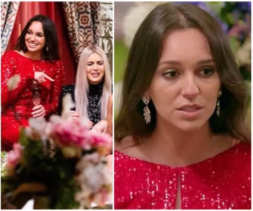 A woman in a sparkling red dress with long earrings sits indoors, smiling, while another woman nearby has a surprised expression.