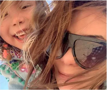 A woman in sunglasses and a smiling child with windblown hair enjoy a sunny day at the beach.