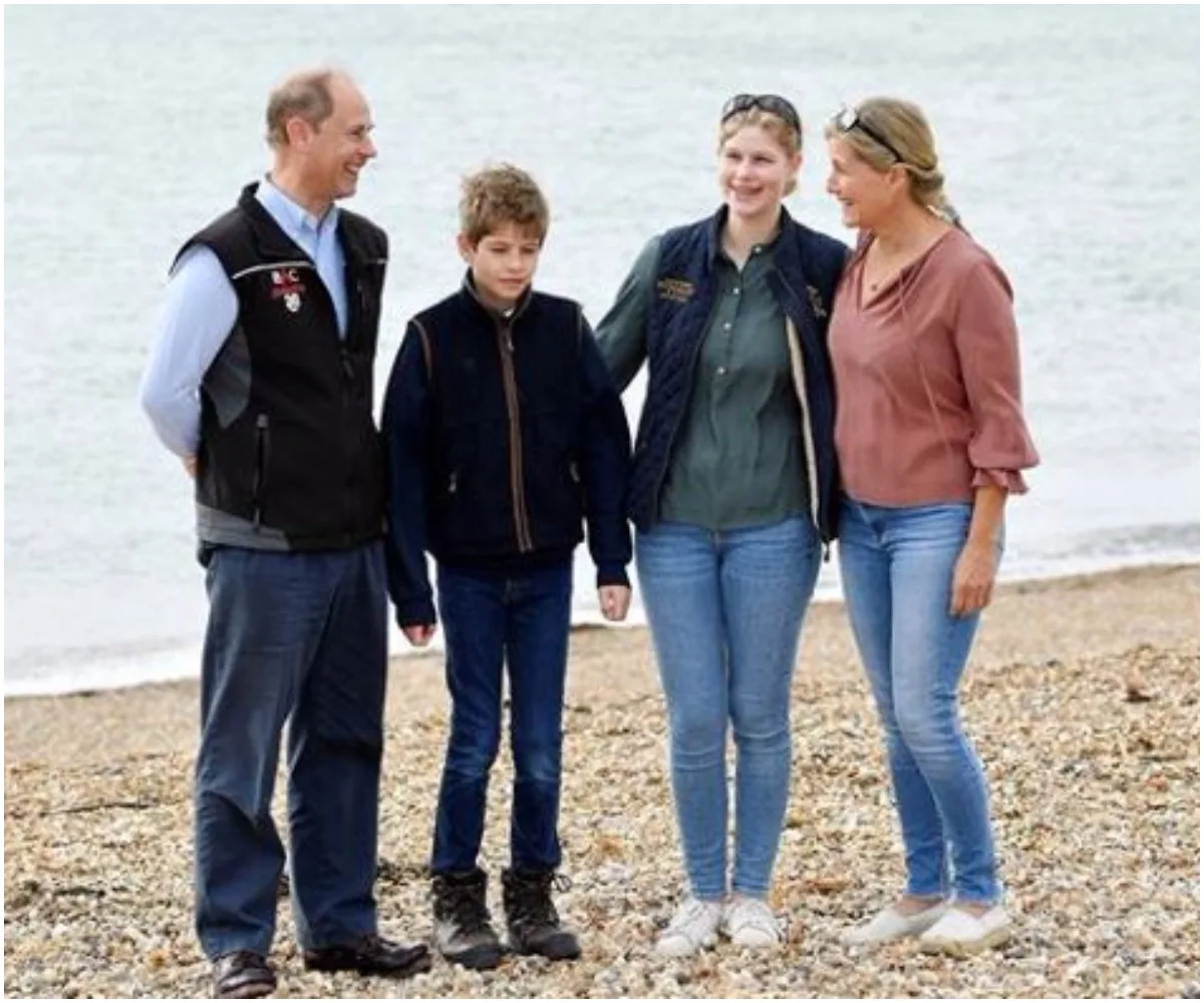 Family of four smiling on a pebble beach, with the sea in the background, dressed casually in outdoor wear.