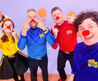 The Wiggles group smiling with red noses, featuring members in colored shirts against a playful background.