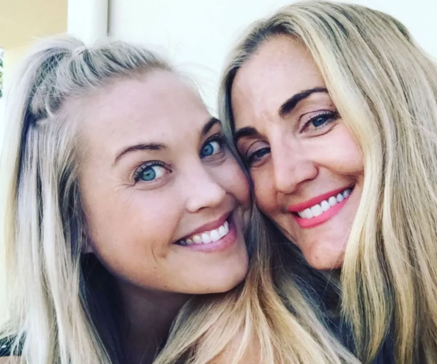 Two smiling women with long blonde hair taking a close-up selfie against a light background.