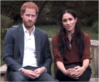 A couple seated on a bench outdoors, engaged in conversation, with greenery in the background.