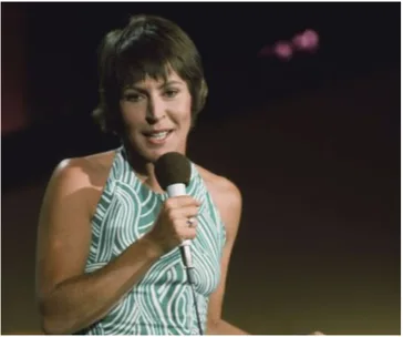 A woman in a green patterned dress holds a microphone while performing on stage.