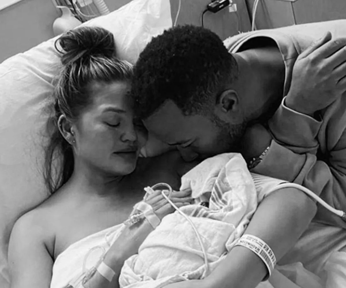 A couple in a hospital bed, comforting each other in a somber moment, with medical equipment visible.