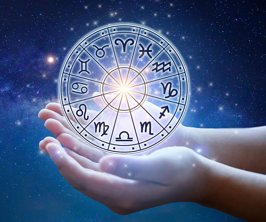 Two hands holding a glowing zodiac wheel against a starry sky.