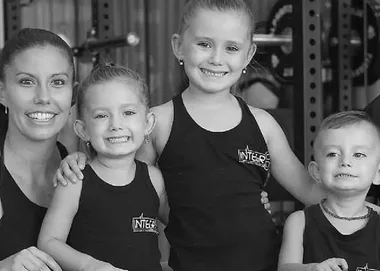 A happy family of four in matching black tank tops, smiling and posing in a gym setting.