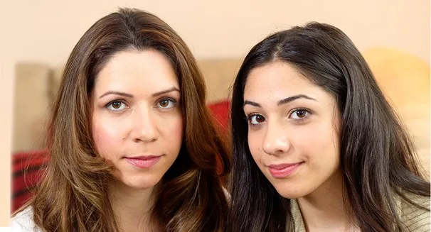 Two women sitting close together, looking at the camera with neutral expressions.