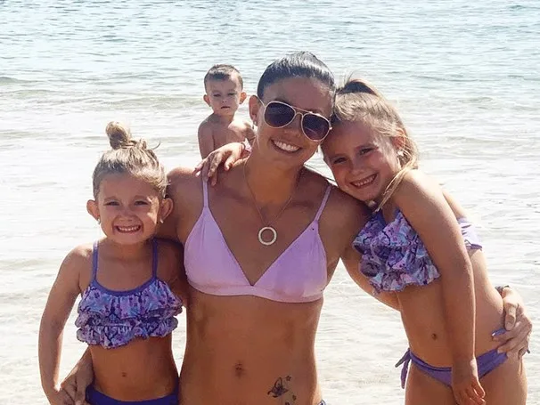 Family enjoying a day at the beach, with a mother and three children smiling and posing by the water.