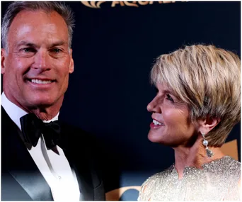 A woman in a glittering dress smiles at a man in a tuxedo at a formal event, with a dark background.