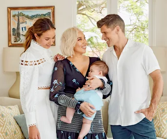 Family smiling and holding a baby in a cozy home setting.
