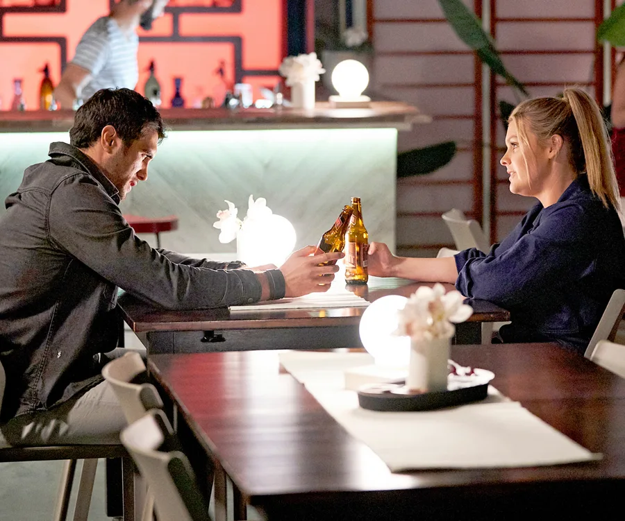 Ziggy and Tane sharing a drink at a dimly lit bar table in a romantic scene from "Home and Away."