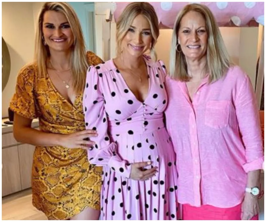 Three women pose together; the center wears a pink polka dot maternity dress, others in pink and yellow dresses.