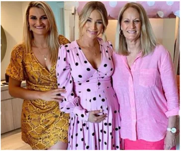 Three women pose together; the center wears a pink polka dot maternity dress, others in pink and yellow dresses.