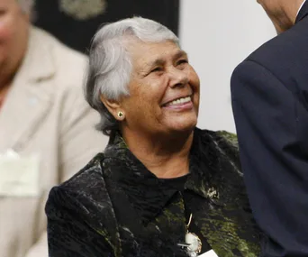 Smiling woman facing a person in a formal setting.