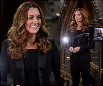 "Person in a black blazer smiling and speaking at an event, lighting equipment visible in the background."