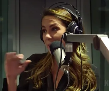 Radio host wearing headphones, speaking into a microphone in a studio setting.