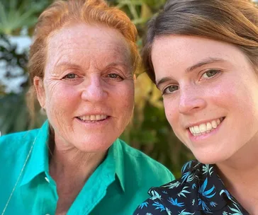 Two women smiling in a close-up selfie outdoors, one wearing a green shirt, the other with a patterned top.