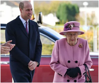 Elderly woman in pink coat and hat, standing with a younger man in a suit, near a red car.