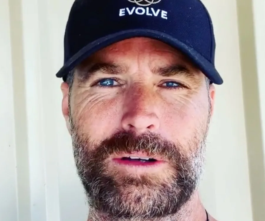 Man with a beard wearing a black cap with "EVOLVE" written on it, looking into the camera.