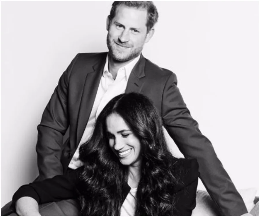 Black and white portrait of a couple smiling; the man stands behind the seated woman.