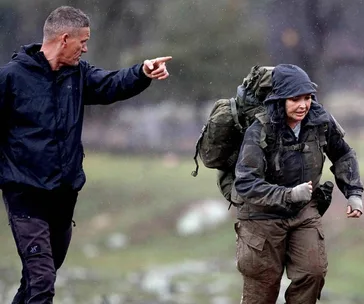 Instructor pointing at a person running with a backpack in the rain during a survival challenge.