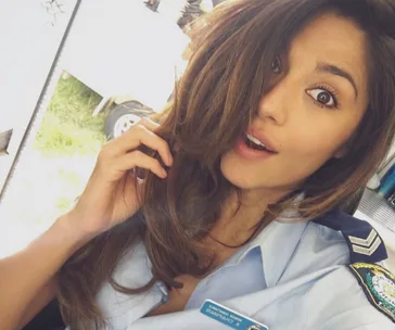 Actor in police uniform from "Home and Away," with surprised expression, holding hair back with one hand.