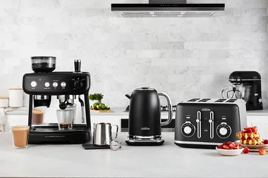 Sunbeam Black Classics collection: espresso machine, kettle, and toaster on a kitchen counter with cups and waffles.