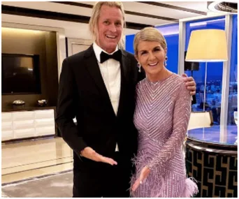 A woman in a sparkling, patterned dress and a man in a black tuxedo smiling in a modern room.