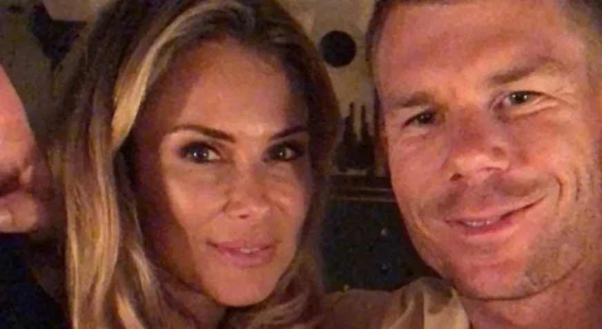 Two people smiling at the camera in a dimly lit setting.