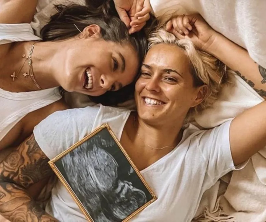 Couple lying down smiling, holding an ultrasound image, symbolizing a pregnancy announcement.
