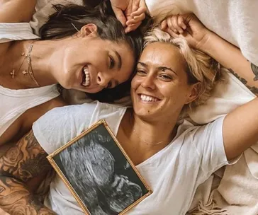 Couple lying down smiling, holding an ultrasound image, symbolizing a pregnancy announcement.