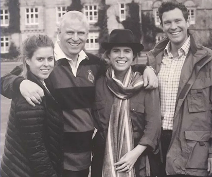 Group of four smiling people outdoors in front of a large building; black and white photo.