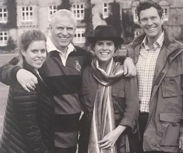 Group of four smiling people outdoors in front of a large building; black and white photo.