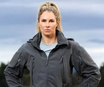 Woman in outdoor gear stands confidently with hands on hips against a cloudy sky.