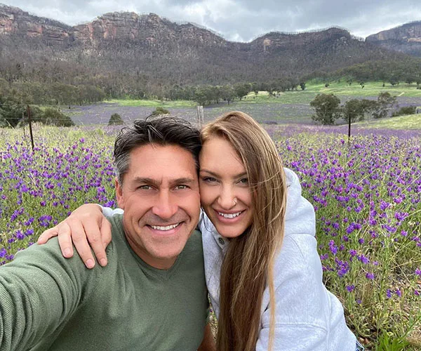 Couple smiling in a field of purple flowers with mountains in the background.