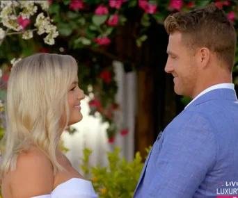 A couple smiling at each other under a floral arch.