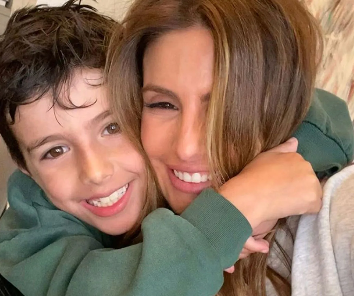 Mother and son smiling joyfully, with the son hugging the mother closely at home.