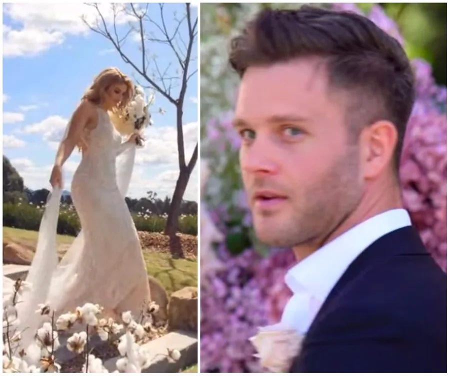 Bride walking outdoors in wedding dress; groom in suit looking back near pink flowers.