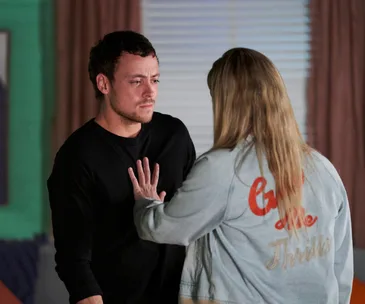 Two people in a tense moment, one with hand on the other's chest, from "Home and Away" scene.