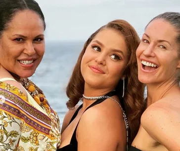 "Three women smiling joyfully at the camera with the ocean in the background."