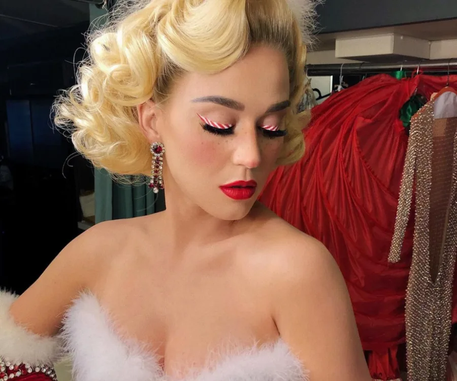 Blonde woman in festive makeup and outfit with red lipstick and curled hair, wearing dangling earrings.