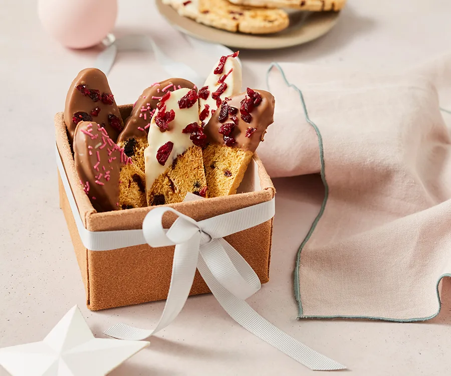 Christmas biscotti with chocolate, cranberries in a gift box, wrapped with a ribbon, on a soft pink surface.
