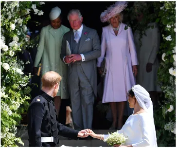 "Wedding guests watch as bride and groom hold hands under floral archway."