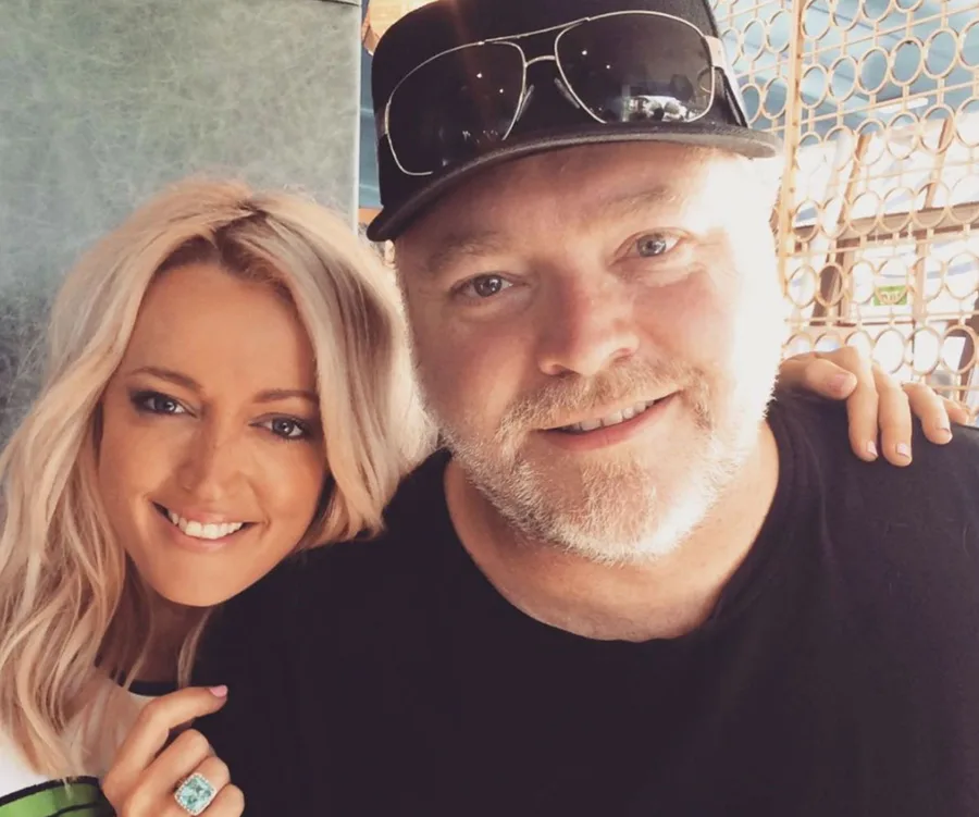 Two people smiling, one wearing a cap and sunglasses on head; casual setting.