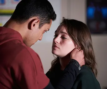 A man and woman in an emotional moment, facing each other closely, indoors.