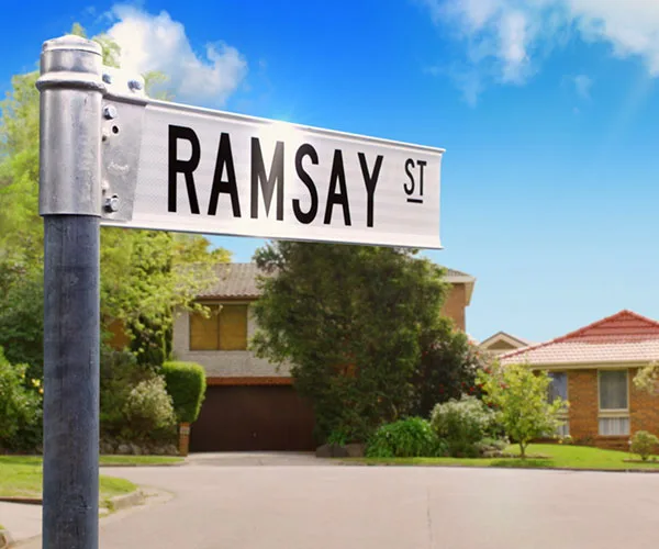 "Ramsay Street sign from the show 'Neighbours' with suburban houses in the background on a sunny day."
