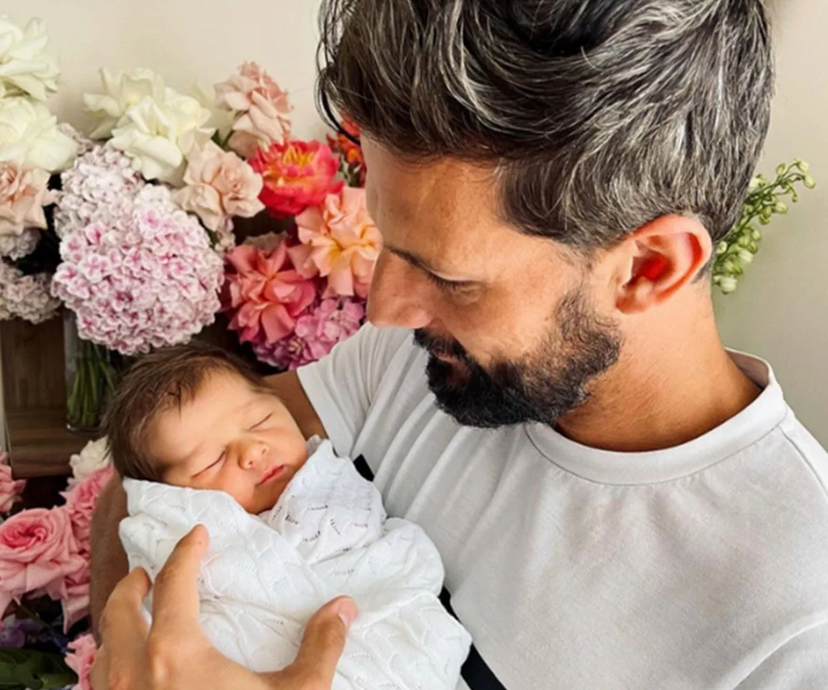 Man holding a sleeping baby surrounded by colorful flowers.