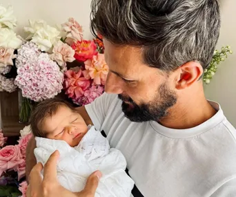 Man holding a sleeping baby surrounded by colorful flowers.