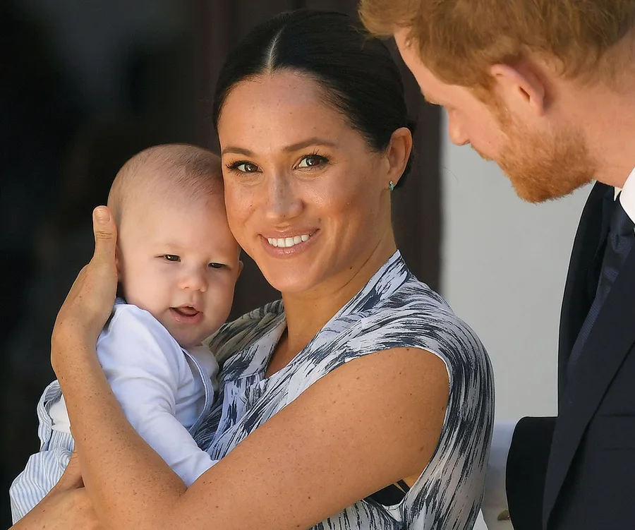A woman smiling while holding a baby, with a man looking on, all appearing joyful and engaged.